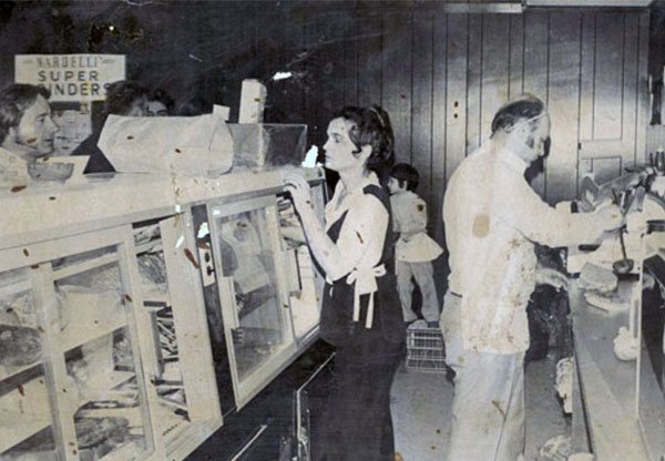 1979 Rina and Joe wait on customers in their Naugatuck store. Their son, Marco (3rd generation), is standing on a milk crate at the register, closing sales.